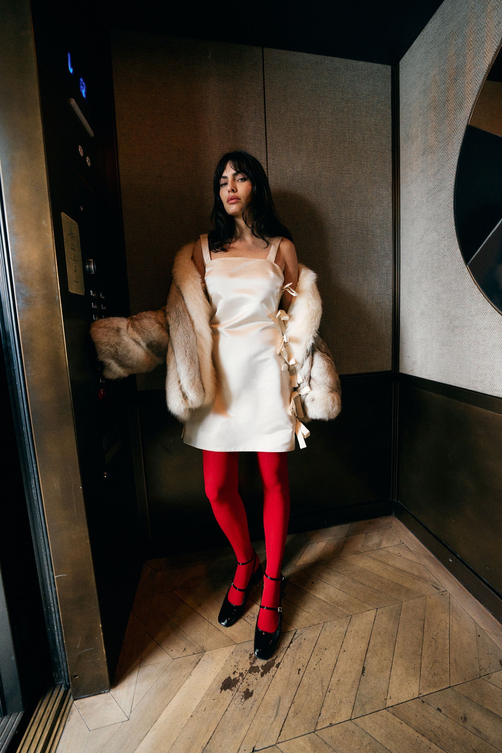 woman riding on elevator in white wedding dress with fur coat and red leggings