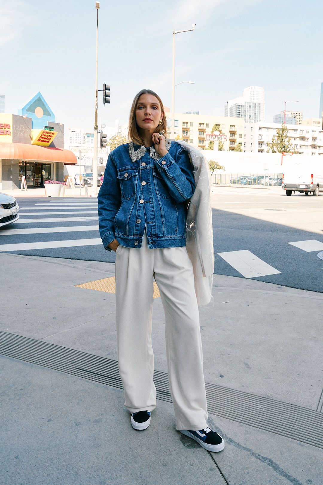 woman on street corner with jean jacket and white pants